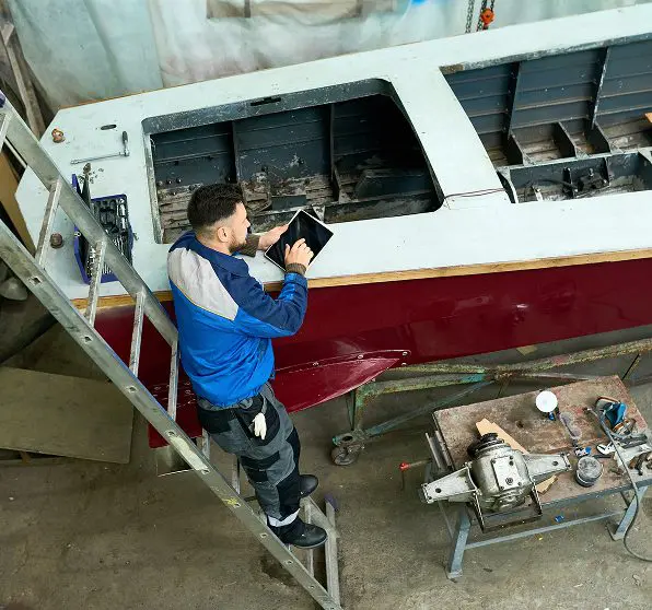 Man inspecting boat on ladder in workshop.