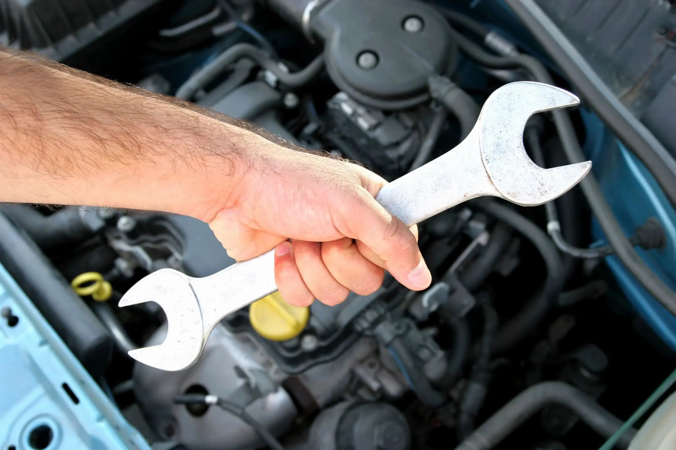 Hand holding wrench working on car engine.